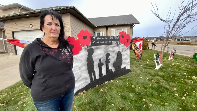 A woman stands on her front lawn in front of a  Remembrance Day display. 