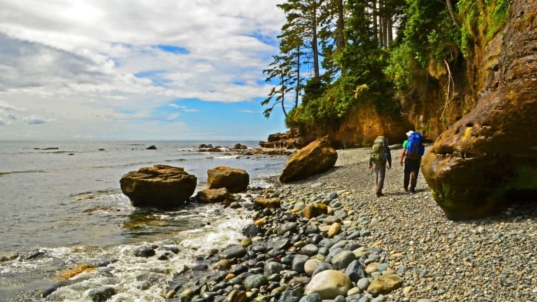 Two people walk along a rocky shoreline