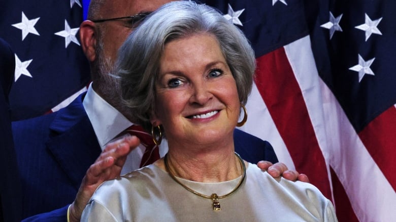 A grey-haired woman smiles in the centre of the image. 