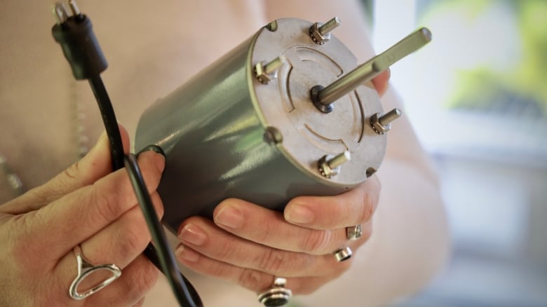 A person holds a silver cylindrical electrical component about the size of a yogurt tub.