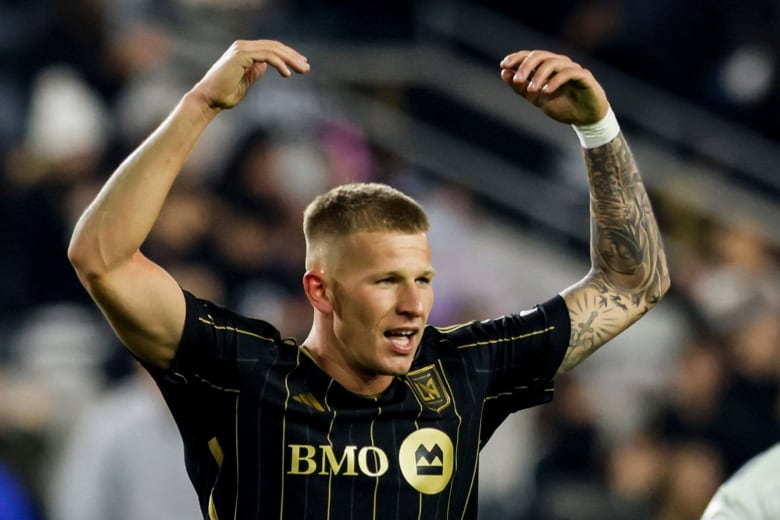 A soccer player raises his hands in the air in celebration.