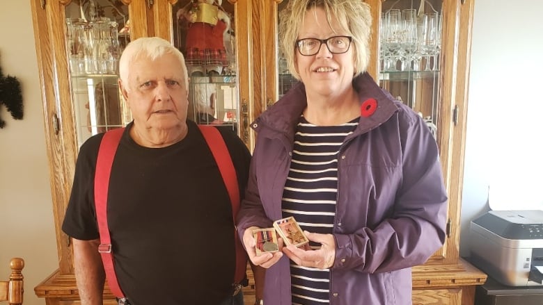 A woman poses with an elderly man. She is holding two war medals in their cases.