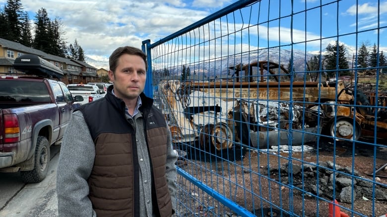 Man standing outside of a fenced-off area containing wildfire debris in Jasper