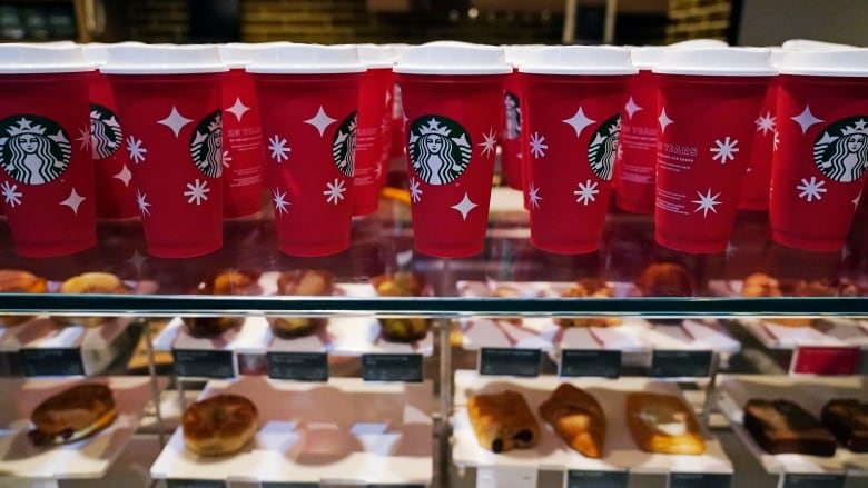 Red holidays Starbucks cups in a  line on a display case of baked goods