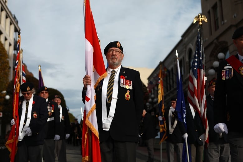 A man in a suit, adorned with medals, carries a flag