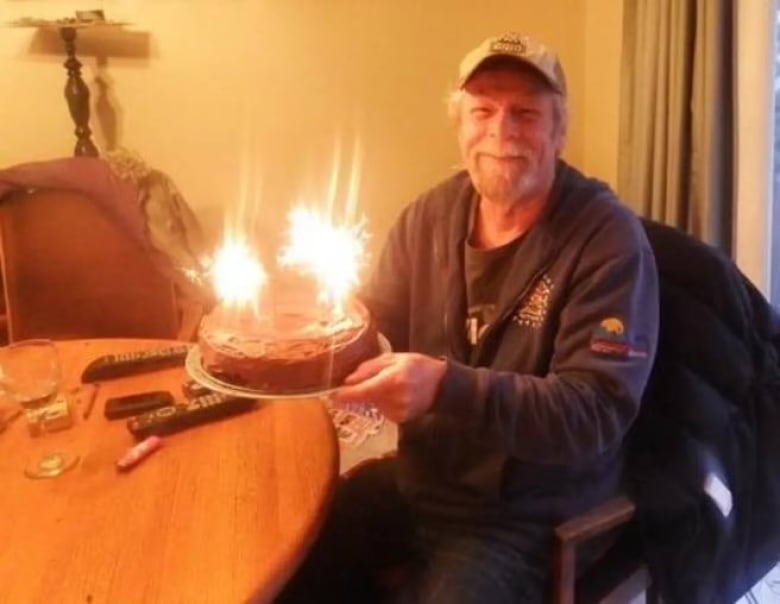 A man holding a birthday cake smiles.