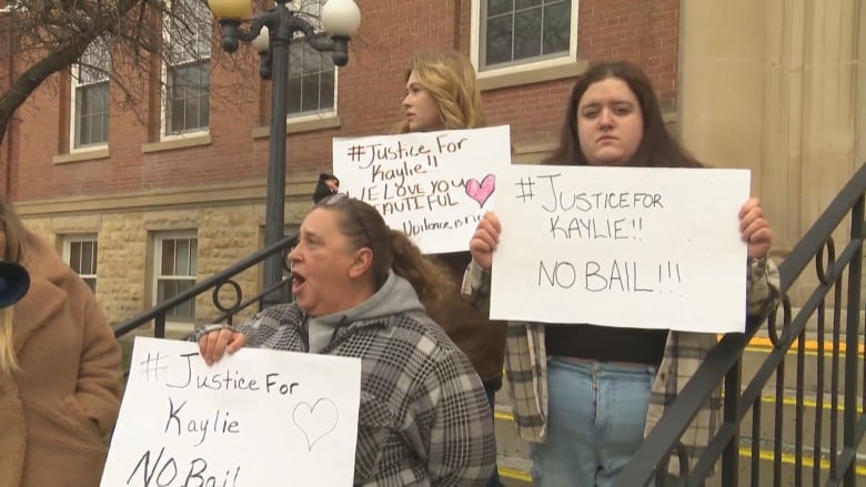 Three people on steps holding signs in protest.