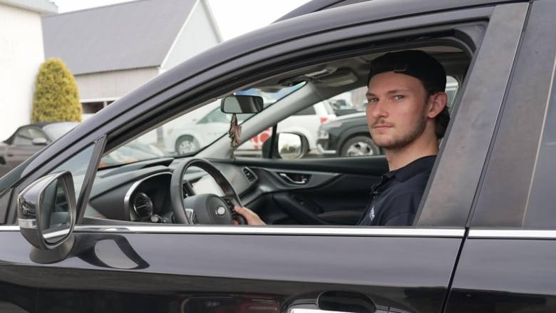 A man sits in the driver's seat of a black car.