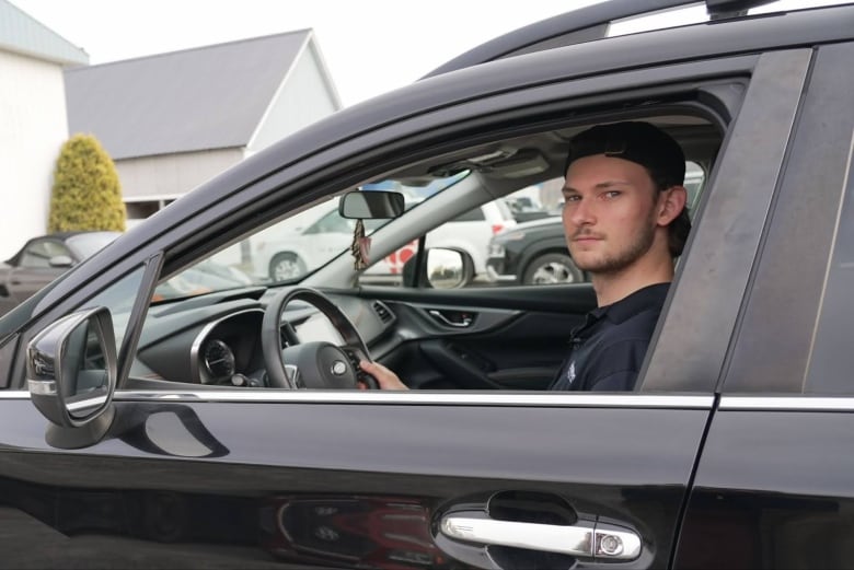 A man sits in the driver's seat of a black car.