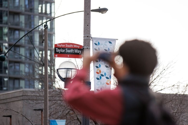 A person takes cellphone pic of a newly erected Taylor Swift Way street sign in Toronto.