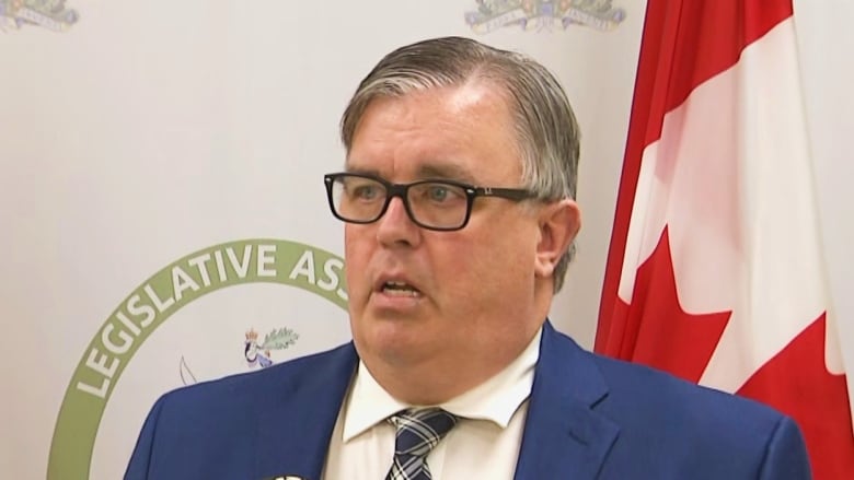 Man with blue jackets and tie standing in front of P.E.I. and Canada flags.