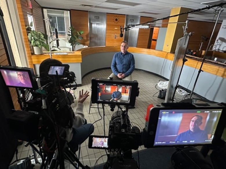 A man sits in a room surrounded by camera equipment