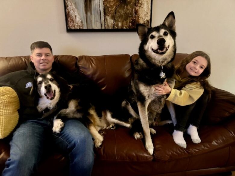 A man sits with a girl and two dogs.