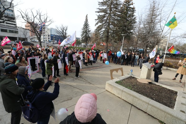 dozens of people are gathered outside with someone speaking at the front 