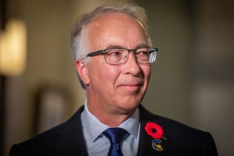 A white man wearing a poppy and a blue pin looks to his left.+