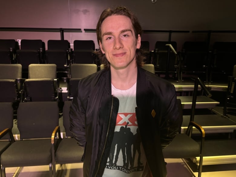 Young man with hands behind his back. There are chairs behind him