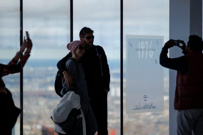 Couple having their photo taken next to a poster that reads: Toronto's version 1976, at the CN Tower's main observation deck.