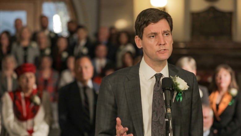 A man talks to a mic while surrounded by a number of people.