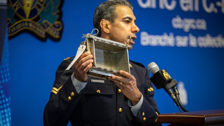 An officer in uniform holds up a square box.