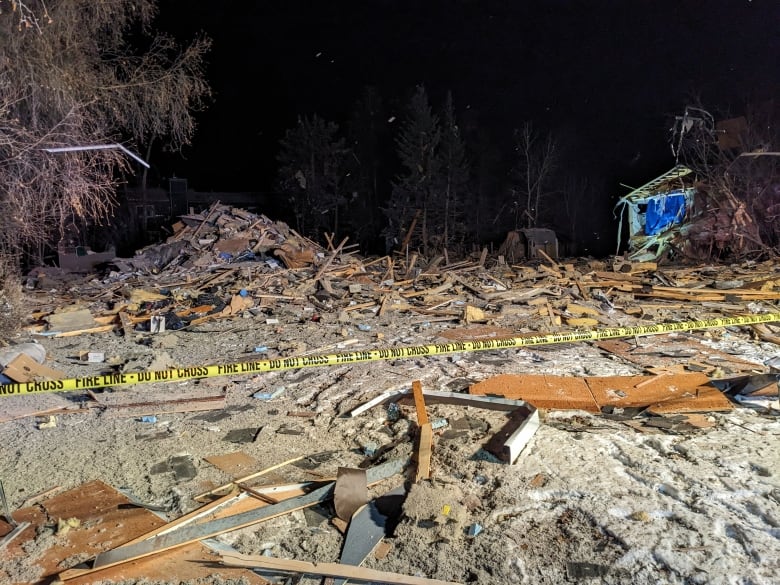 A pile of rubble with police tape. A damaged house in the background. 