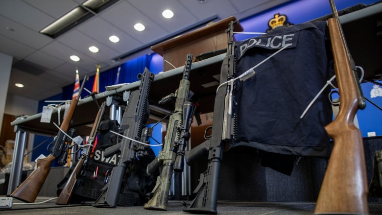 A row of rifles lean against a police table, along with police vests.