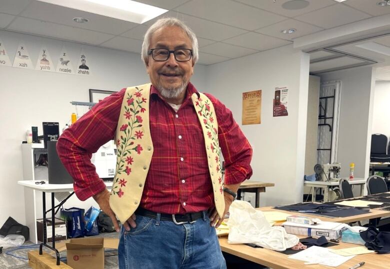 A smiling man poses for a photo in a vest with embroidered flowers on it.