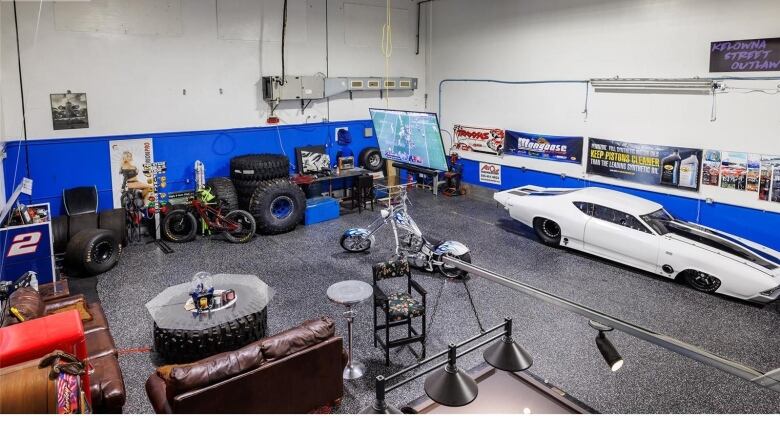 An industrial space is filled with couches, motorcycles, a sports car, a TV and posters. 