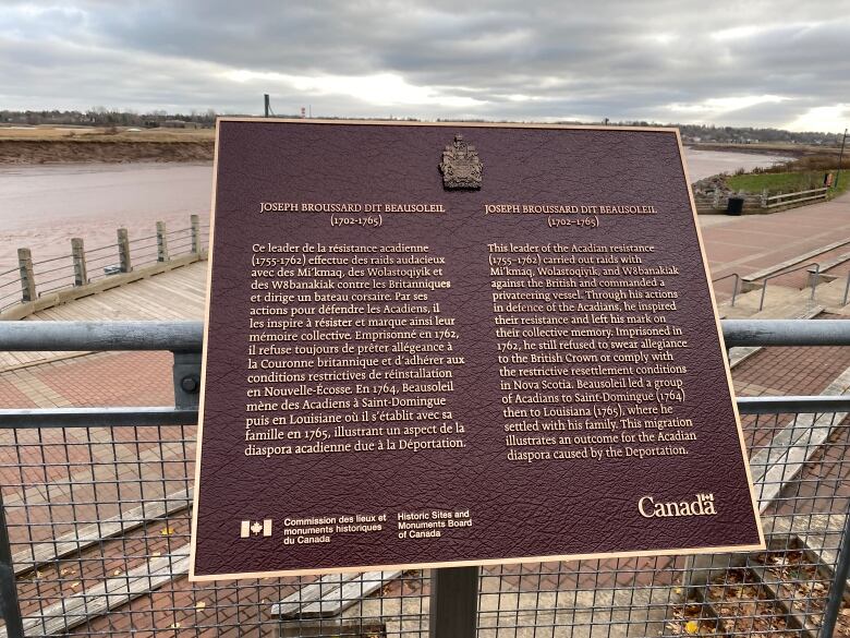 A plaque with a purple background and gold text, in front of a walkway and river.