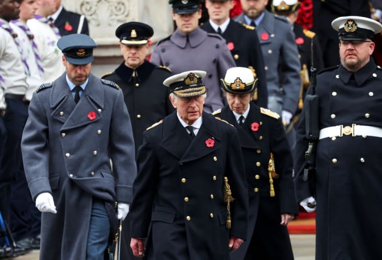 Several people wearing long military coats walk ahead.