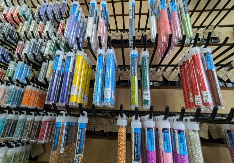 Tubes of different coloured beads hanging on a peg board in a store.