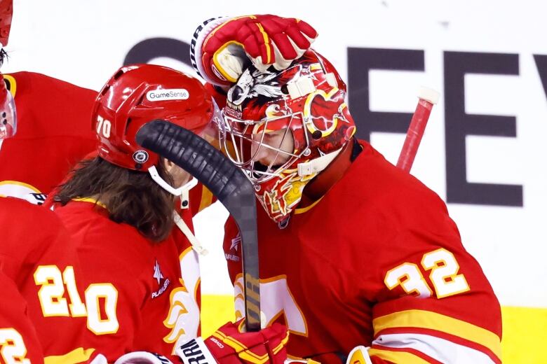 Two hockey players wearing helmets and masks are pictured tapping their heads together. 