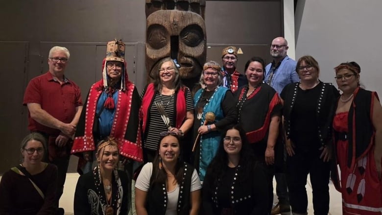 A group of people inside a museum standing in front of a totem pole.