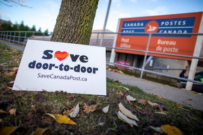 A sign reading 'Save door-to-door savecanadapost.ca' is pictured next to a Canada Post office.