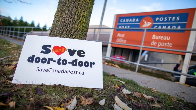 A sign reading 'Save door-to-door savecanadapost.ca' is pictured next to a Canada Post office.