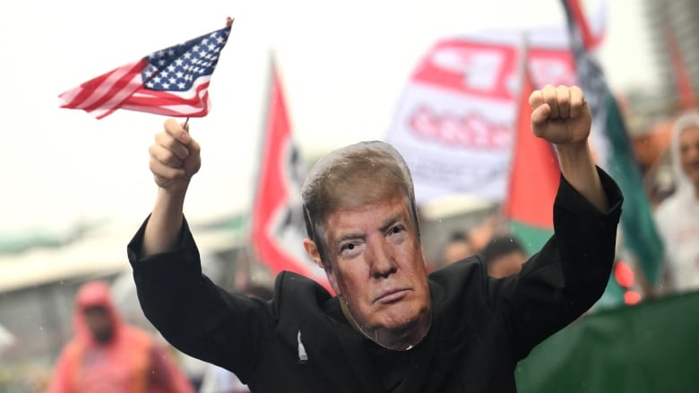 A demonstrator waves a mini U.S. flag and wears a mask featuring another person's face.