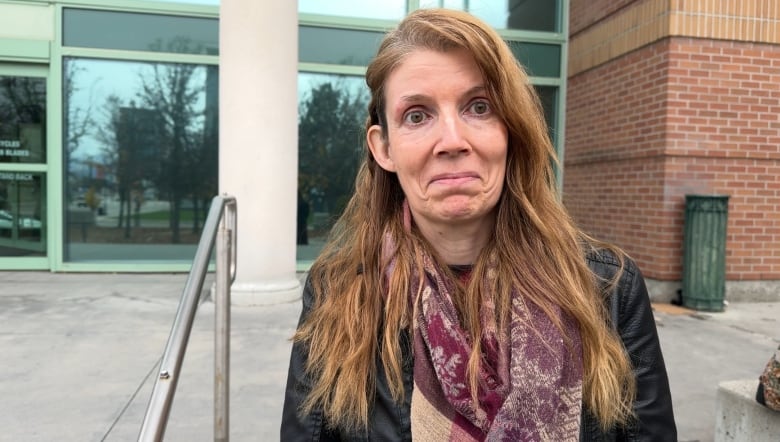 A slim, middle-aged woman with long, red hair wearing a scarf and a winter jacket in a profile photo on the steps of the Kelowna courthouse.