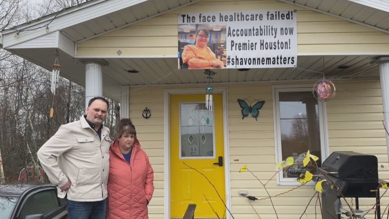 A man and woman are shown outside their home with yellow siding beneath a poster above the door showing a photo of their daughter Shavonne.