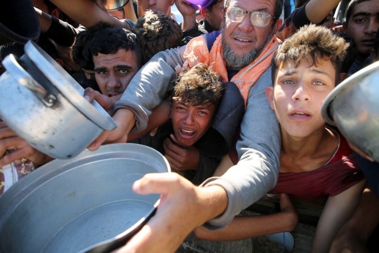 Young boys and a man stick out their arms with pots in hand.