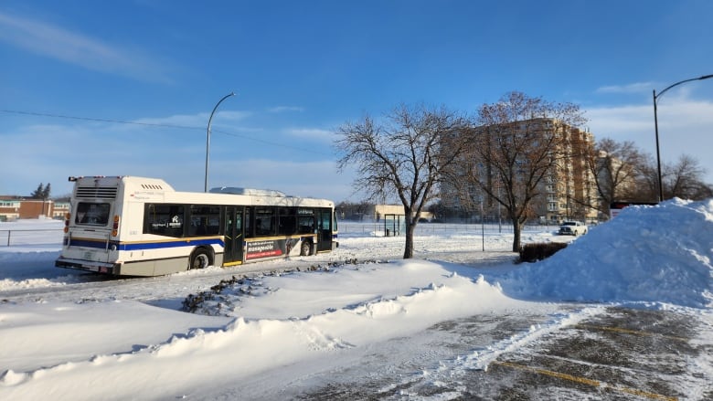 A city bus sits crooked on a snowy street.