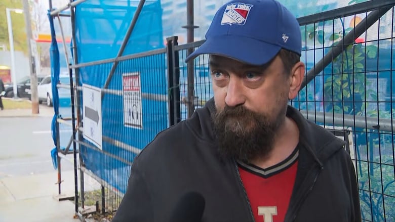 A man with a beard wearing a baseball cap speaks to a reporter. 