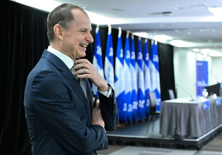 Man in suit smiles with Quebec blue and white flags behind him.