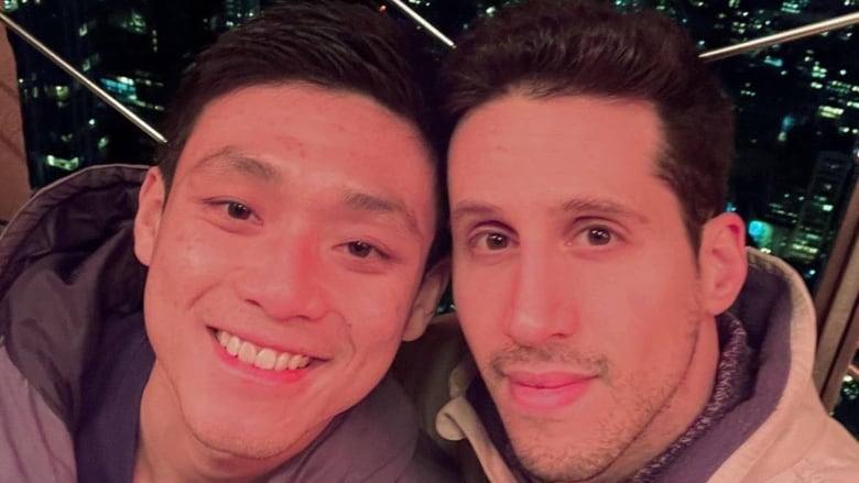 An Asian man smiles for a photo next to another man who looks into the camera.