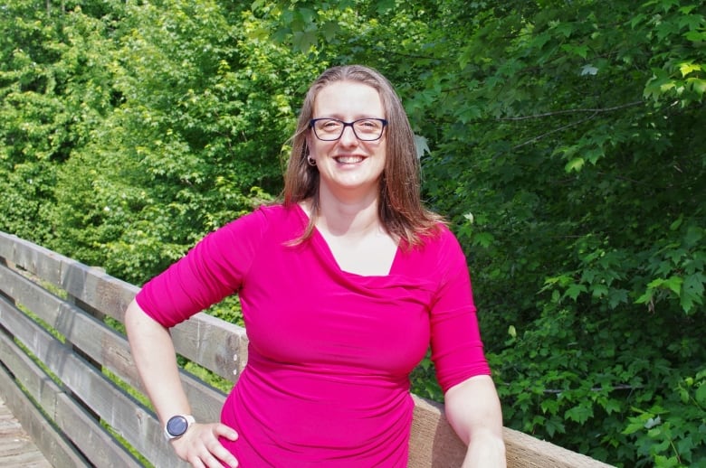 A woman wearing a pink shirt smiles for a photo.