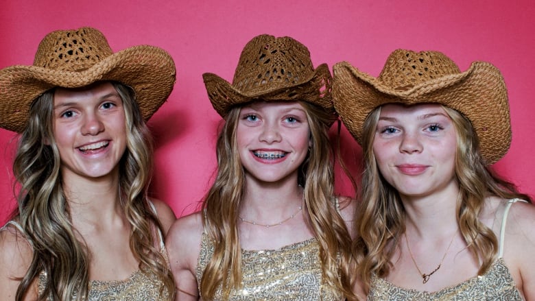 Three young blonde girls pose for a portrait in same gold sequin strappy tops and straw cowboy hats