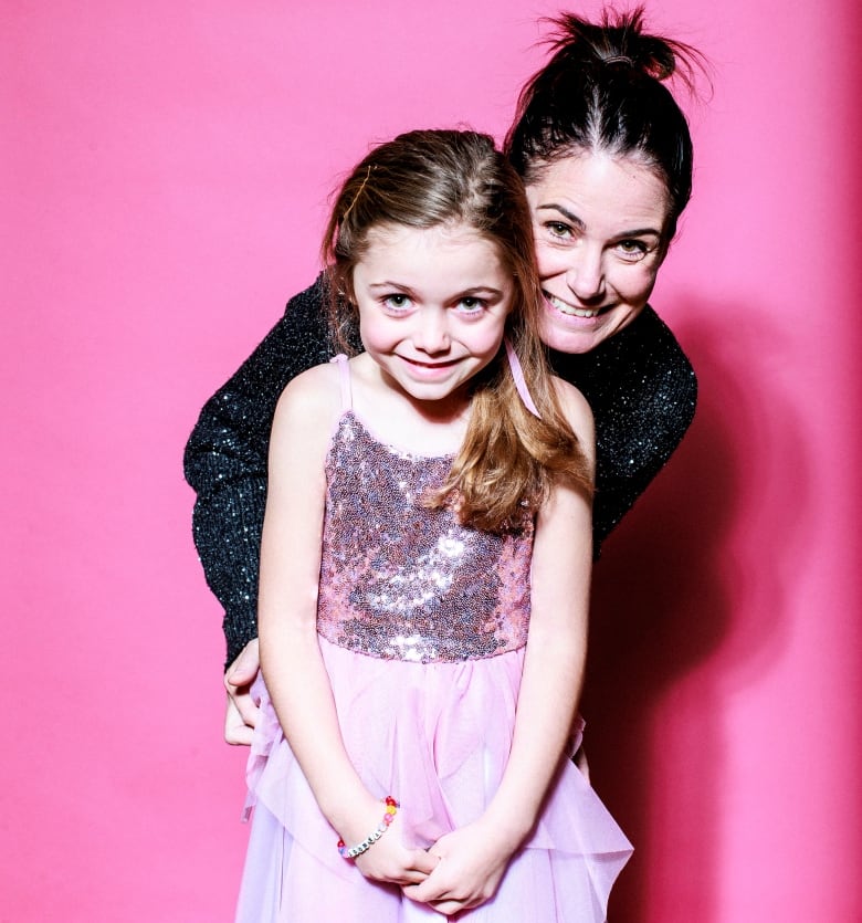 A mom and daughter pose for a portrait wearing sequin outfits, against a pink background.