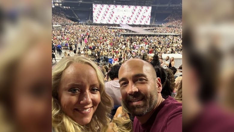 A woman and a man sit smiling in the stands with a stage behind her.