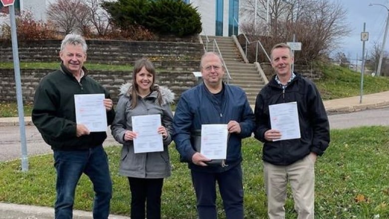 Four people each hold a paper outside a courthouse 