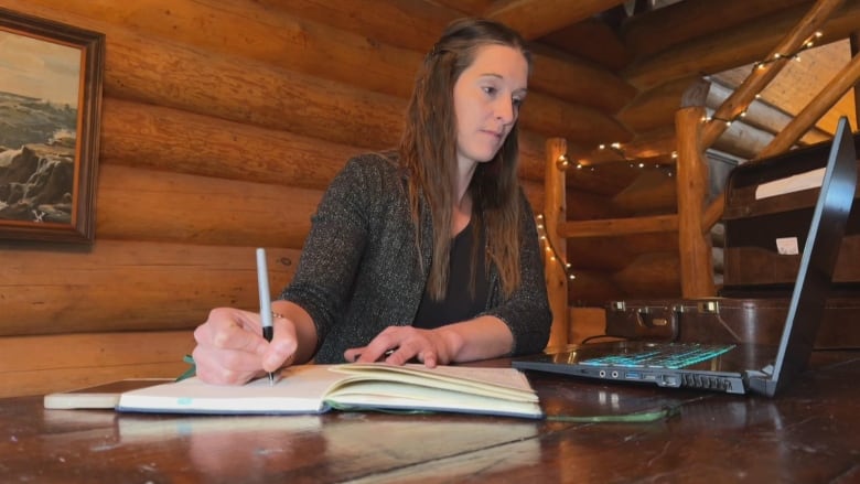 a woman writes while looking at a computer screen 