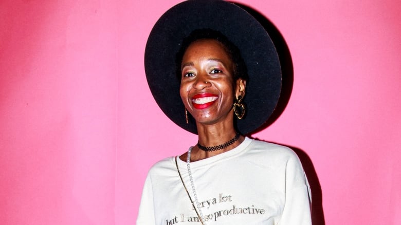 A Black woman wearing a black hat and white. sweatshirt that reads: I cry a lot but I'm so productive.