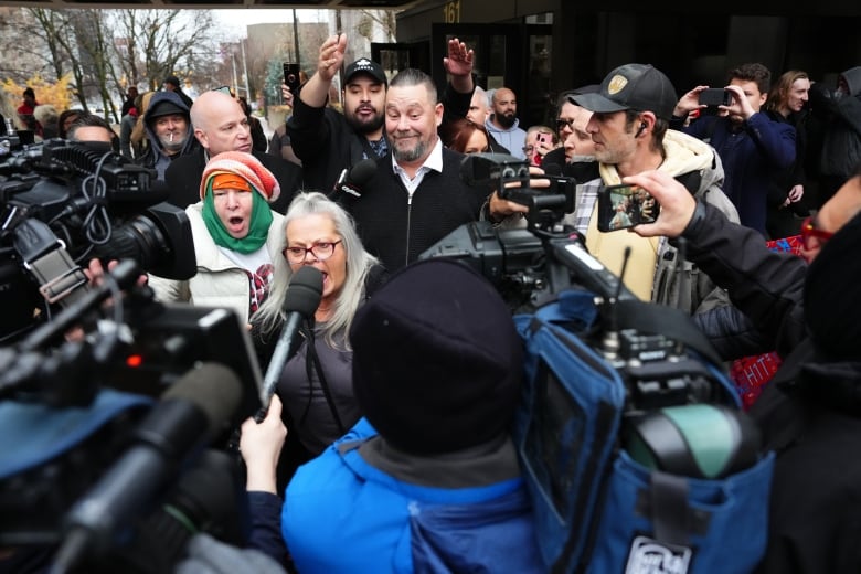 A man surrounded by supporters as he leaves a courthouse in autumn.